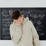 A frustrated student in a classroom standing in front of a blackboard filled with trigonometry equations.
