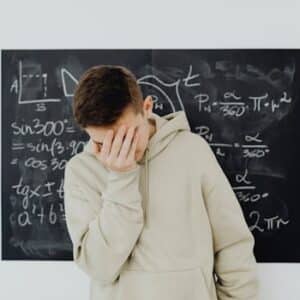 A frustrated student in a classroom standing in front of a blackboard filled with trigonometry equations.
