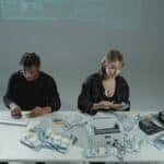 Two people counting money at a desk with computers and cash equipment.