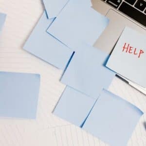 A cluttered workspace with sticky notes on a laptop, symbolizing overwhelm and need for help.