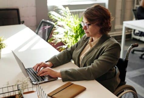 Businesswoman in wheelchair using laptop at office desk.