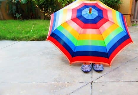 Bright and colorful rainbow umbrella shading patterned shoes on a sunny day.