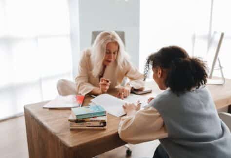 A tutor and student engaged in a learning session with books and notes on a table.