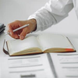 Close-up of a businessman writing notes in a diary at a modern office desk.