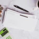 Flat lay of financial documents, calculator, coins, and coffee cup on marble surface.