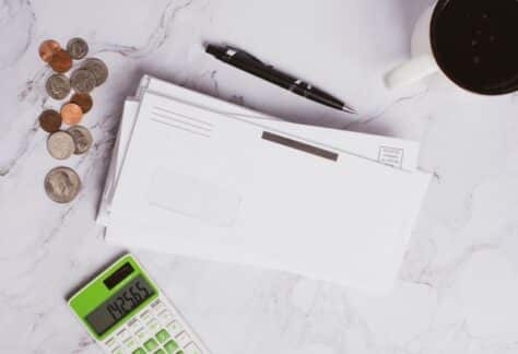 Flat lay of financial documents, calculator, coins, and coffee cup on marble surface.