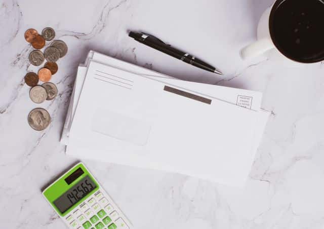 Flat lay of financial documents, calculator, coins, and coffee cup on marble surface.